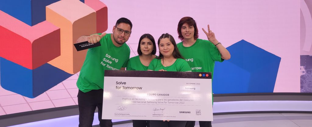 Grupo de quatro jovens usando camisetas verdes com o logo "Samsung Solve for Tomorrow", segurando um cheque simbólico de premiação. Eles sorriem e fazem gestos de vitória, simbolizando conexão.
