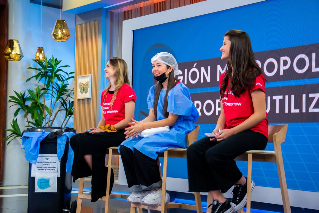Professora e duas jovens sentadas em palco do Solve for Tomorrow